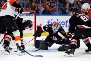 Dec 18, 2025; Buffalo, New York, USA; Buffalo Sabres center Josh Norris (9) and goaltender Alex Lyon (34) look to clear the puck during the third period against the Philadelphia Flyers at KeyBank Center.