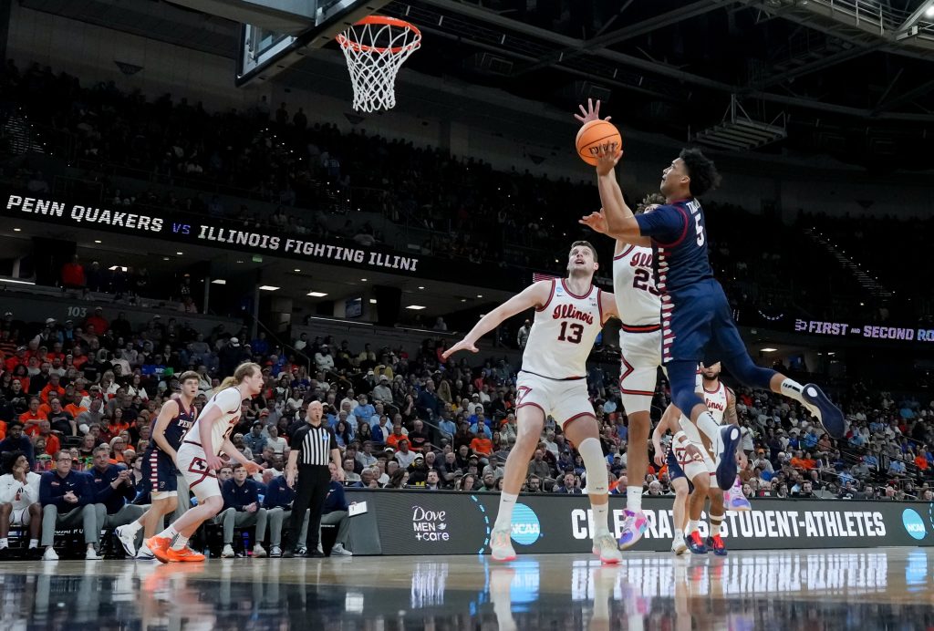 Mar 19, 2026; Greenville, SC, USA; Penn Quakers guard Cam Thrower (5) shoots past Illinois Fighting Illini guard Keaton Wagler (23) in the first half of a first round game of the men's 2026 NCAA Tournament at Bon Secours Wellness Arena.