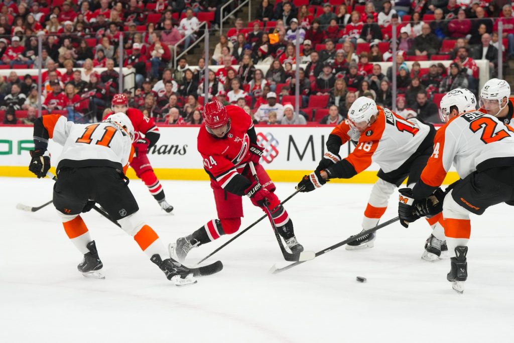 Dec 14, 2025; Raleigh, North Carolina, USA; Carolina Hurricanes center Seth Jarvis (24) takes a shot against Philadelphia Flyers center Rodrigo Abols (18) and right wing Travis Konecny (11) during the first period at Lenovo Center.