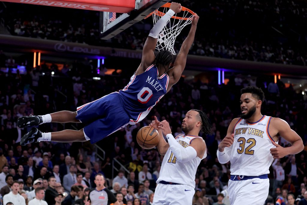 Oct 20, 2026; New York, New York, USA; Philadelphia 76ers guard Tyrese Maxey (0) hangs on the rim after a dunk against New York Knicks guard Jalen Brunson (11) and center Karl-Anthony Towns (32) during the fourth quarter at Madison Square Garden. Mandatory Credit: