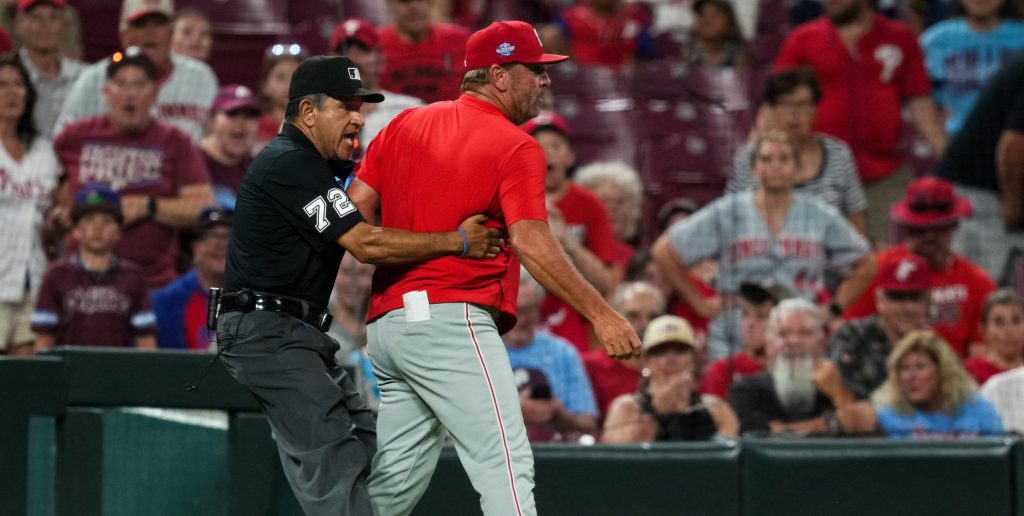 Jul 7, 2026; Cincinnati, Ohio, USA; Umpire Alfonso Márquez (72) attempts to hold back Philadelphia Phillies infield coach Bobby Dickerson (9) as he rushes the field towards umpire Lance Barrett (16) during the game against the Cincinnati Reds in the eighth inning at Great American Ball Park.