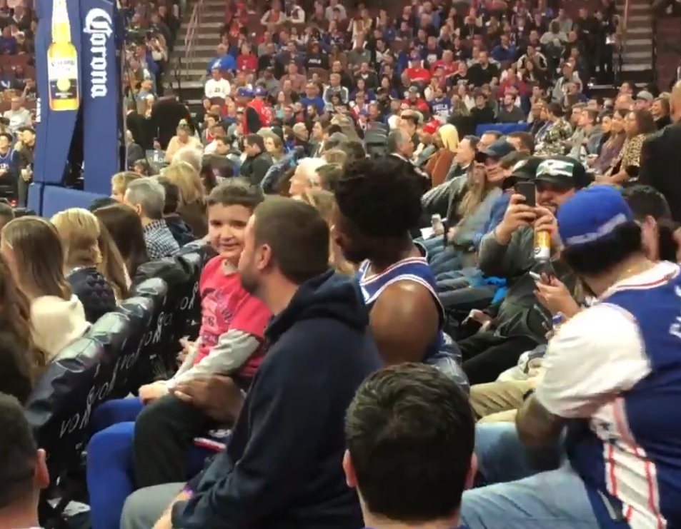 Joel Embiid, Sitting in the Second Row With a Kid on his Lap